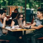 A group of young adults working on a laptop at an outdoor coffee shop, enjoying teamwork and collaboration.