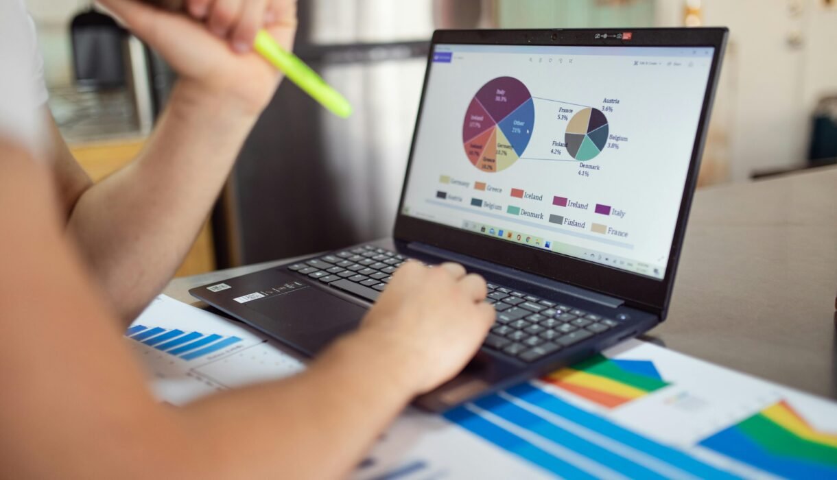 Person analyzing financial charts and graphs on a laptop with colorful documents, showcasing market analysis.